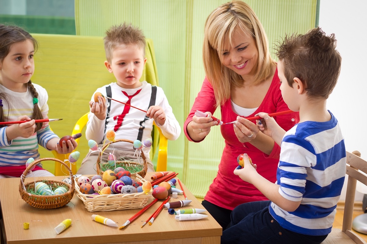 kids painting easter eggs with teacher