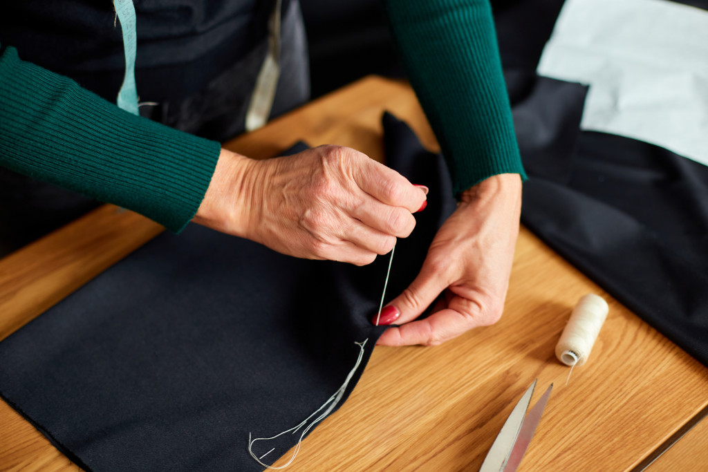 Top view Step by step, 50-yers old woman sewing fabric with hand, Mature tailor working with sewing in atelier, textile industry, hobby, workspace. Creation process DIY, Workplace of seamstress.