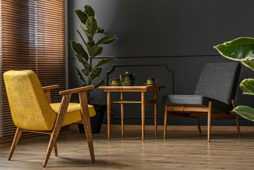 A living area with midcentury-modern-inspired chairs and tables, wooden blinds, and two plants