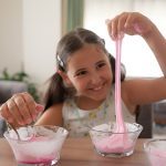 smiling girl stretching butter slime from a bowl